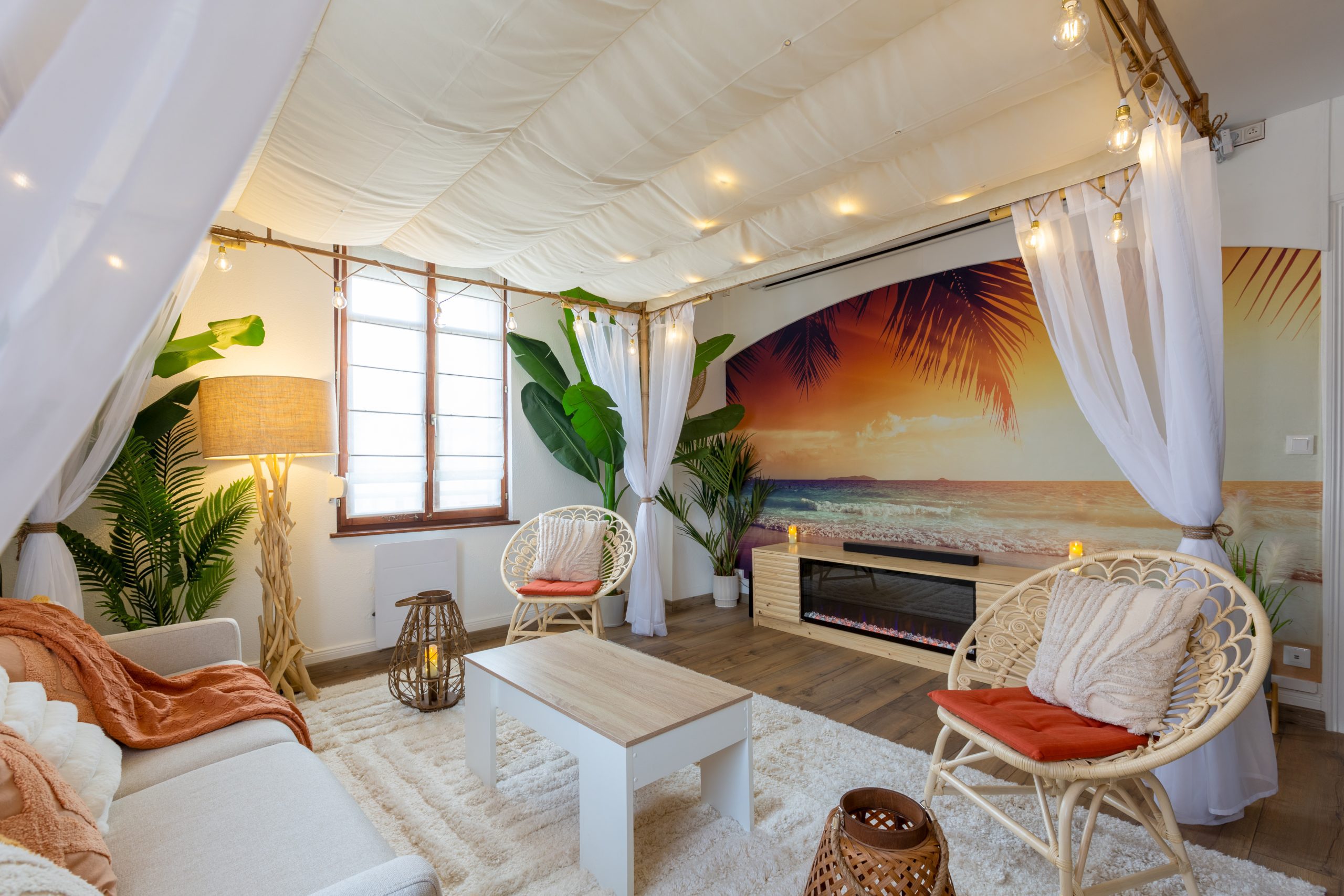 Magnifique décoration du salon sous la pergola entourée de guirlandes lumineuses et de lanternes à bougies led pour profiter en sirotant un cocktail en face du feu de la plage